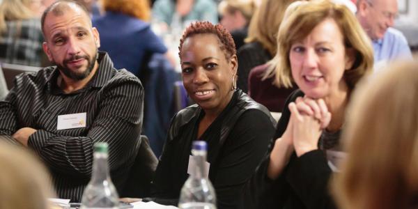 Two women and a man sitting around a table and looking at the camera