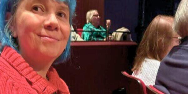 Sarah with Blue Hair and a red coat smiling at the camera