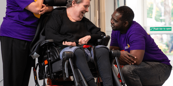 A Caucasian female wheelchair user with two Leonard Cheshire support workers wearing branded t shirts