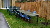 An outside garden space with a long tarmac footpath and a lawn running beside it with a long garden table and chairs