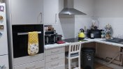An oak laminated kitchen with grey appliances including an oven fridge and cooker with a breakfast bar stool seat and a yellow kettle on top of the surface