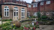 The back of the house with arched windows and doors backing on to a paved garden area housing a pond in the middle with a water feature