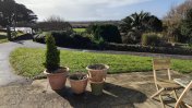 Overlooking view of garden with greenery and a patio area with 4 terracotta plant pots and a wooden garden table and chairs 