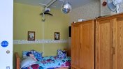 A bedroom with oak style wardrobes and a single bed with a blue flowery duvet with a disco ball hanging from the ceiling and tracking hoists