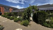 A stone path back garden with shrubs and bushes and an archway surrounded by greenery