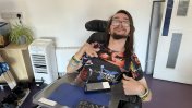A Caucasian male resident with long dark hair and beard and glasses sat in an electric wheelchair smiling 