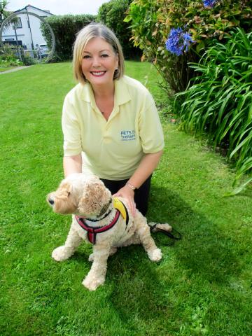 Maggie a caucasian female with blond bobbed hair wearing a yellow polo shirt knelt down on the grass with Bonnie 
