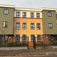An orange and beige block of flats with 3 floors and brown panelled windows on each floor with a black gate in front of the building 